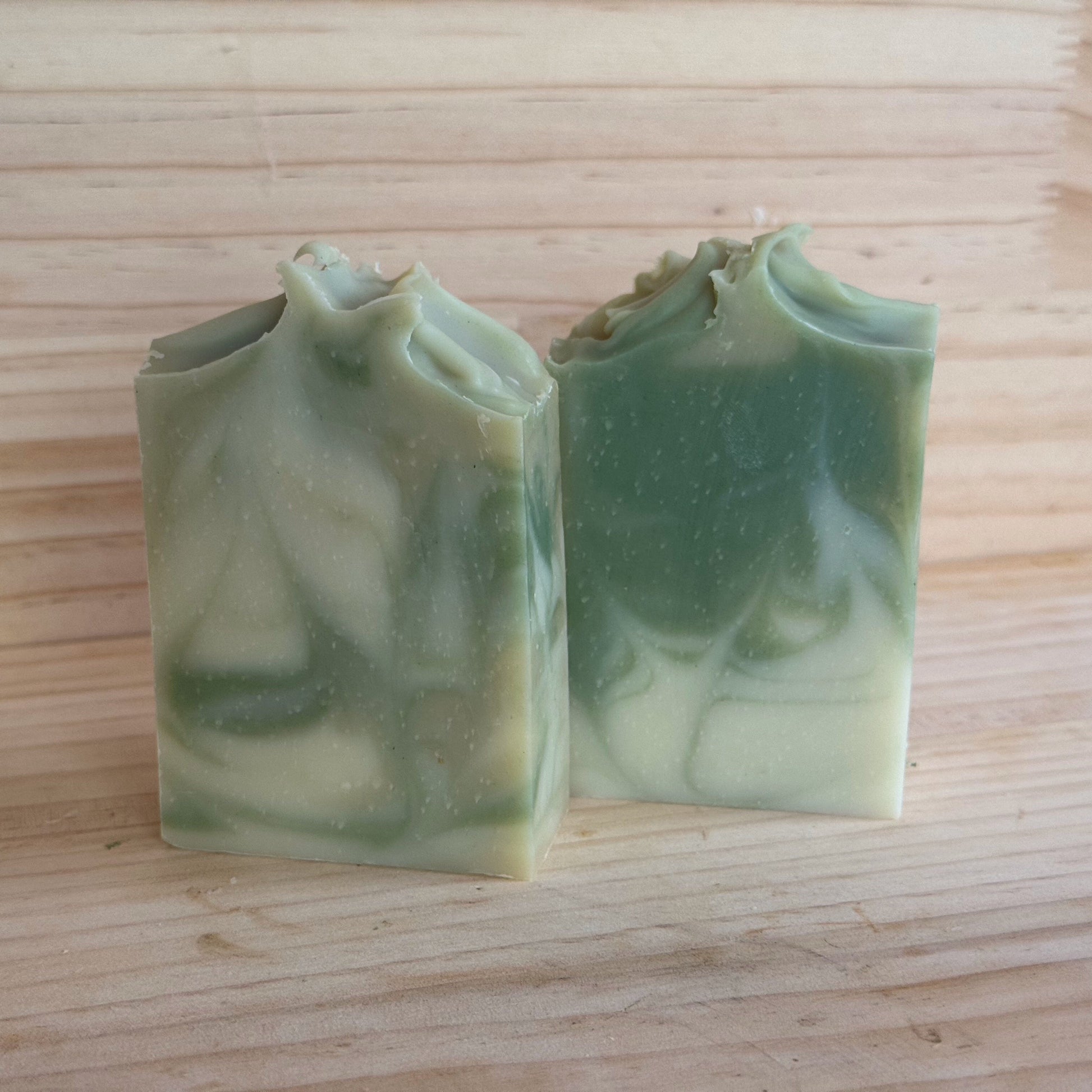 Two green soap bars on a wooden surface