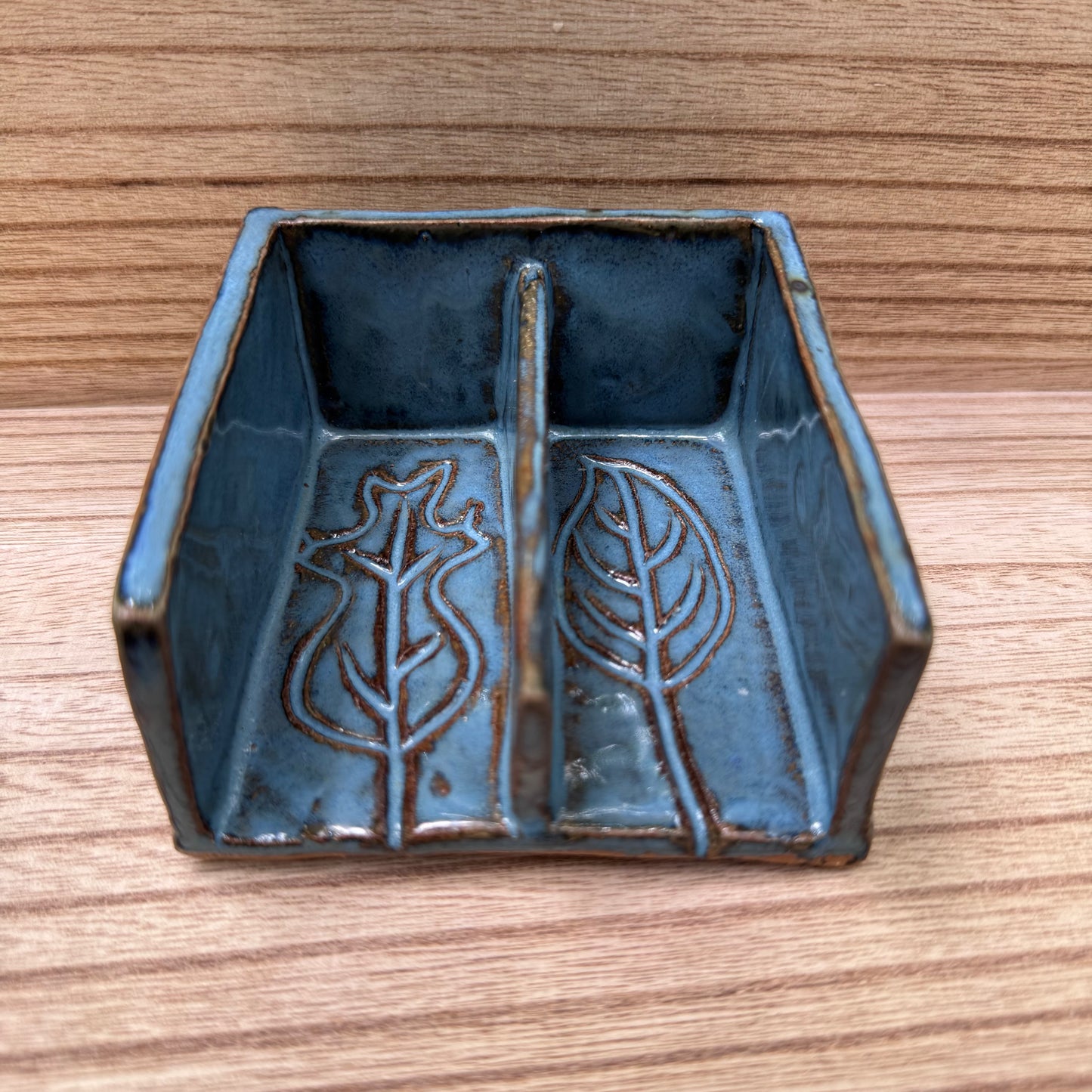 Blue ceramic soap dish with leaf designs on a wooden surface