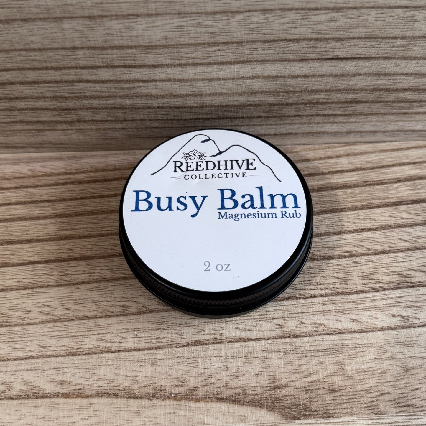 Round container of 'Busy Balm' magnesium rub by Reedhive Collective on a wooden surface
