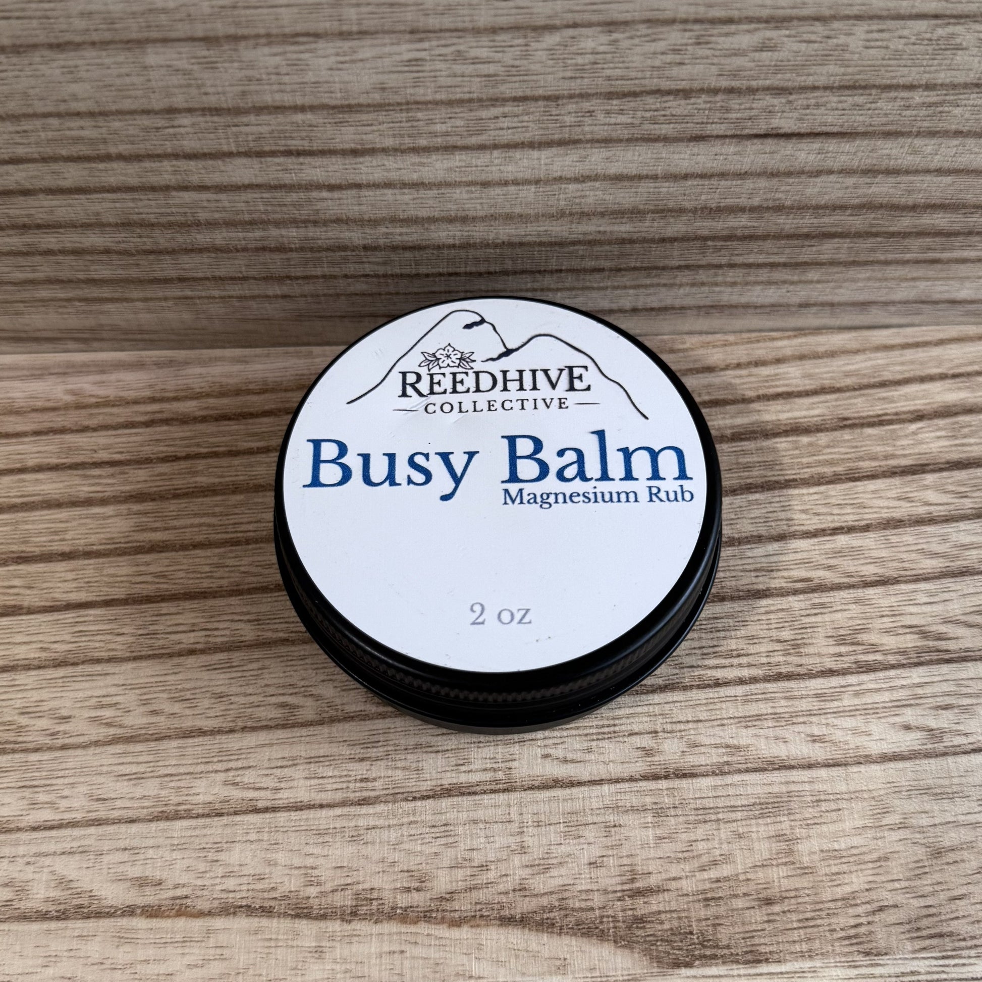 Round container of 'Busy Balm' magnesium rub by Reedhive Collective on a wooden surface
